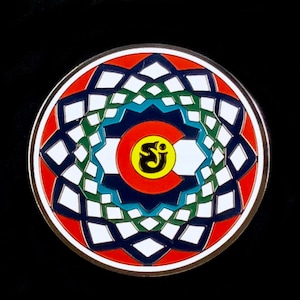 May include: A round, colorful enamel pin with a mandala design. The center of the pin features a yellow circle with a black Om symbol inside. The mandala is made up of concentric circles of red, white, blue, and green.