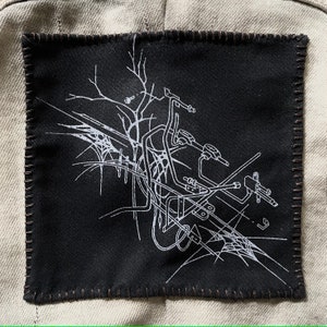 May include: A black fabric patch with white line art depicting a stylized motorcycle design. The patch has a stitched border.