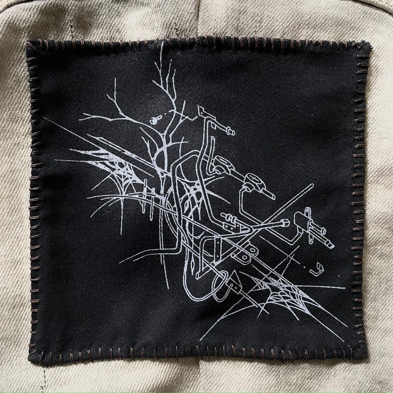 May include: A black fabric patch with white line art depicting a stylized motorcycle design. The patch has a stitched border.
