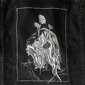 May include: Black denim jacket with a white graphic patch depicting a face with mushroom-like growths. The jacket features black studs on the shoulders and distressed detailing.