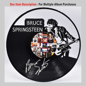 May include: Black vinyl record featuring a silhouette of Bruce Springsteen playing a guitar. The record has a collage of album covers in the centre and his signature below. The text "BRUCE SPRINGSTEEN" is at the top of the record.
