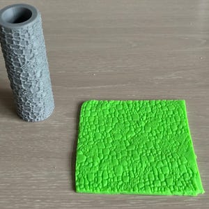 May include: A grey cylindrical tool with a textured surface, alongside a bright green, rectangular piece with a similar textured pattern. These items are likely for crafting or design.