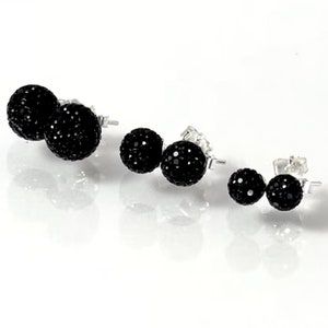 May include: Three pairs of black stud earrings with a sparkly finish. The earrings are different sizes, with the largest pair at the front and the smallest pair at the back.