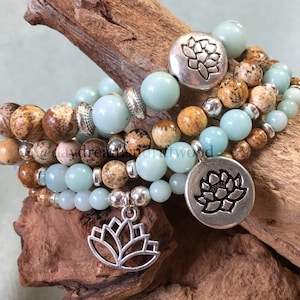 May include: Four layered bracelets with light blue and brown beads and silver lotus flower charms. The bracelets are stacked on a piece of driftwood.