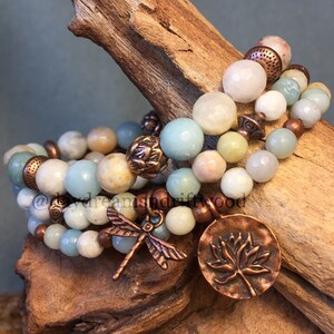 May include: Set of four bracelets featuring aqua, white, and beige gemstone beads with copper accents. The bracelets include a dragonfly charm and a lotus flower charm.