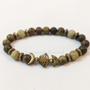 K&ouml;nnte beinhalten: Ein Holzperlenarmband mit einem Metallfisch-Anh&auml;nger. Die Perlen sind in Braun- und Gr&uuml;nt&ouml;nen.