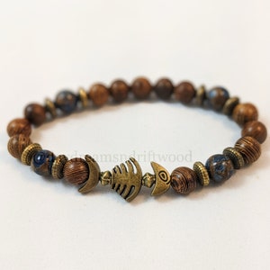 K&ouml;nnte beinhalten: Ein braunes Holzperlenarmband mit einer blau-braunen Perle und einem Fisch-Anh&auml;nger aus Metall.