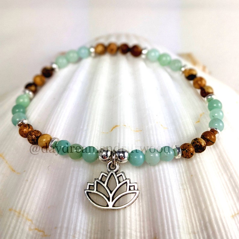May include: A green and brown beaded bracelet with a silver lotus charm. The bracelet is on a white seashell background.