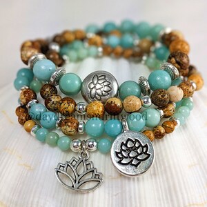 May include: Four layered bracelets with brown and blue beads and silver charms. The charms are lotus flowers. The bracelets are stacked on a white seashell.