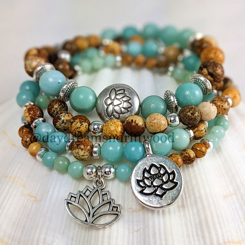 May include: Four layered bracelets with brown and blue beads and silver charms. The charms are lotus flowers. The bracelets are stacked on a white seashell.