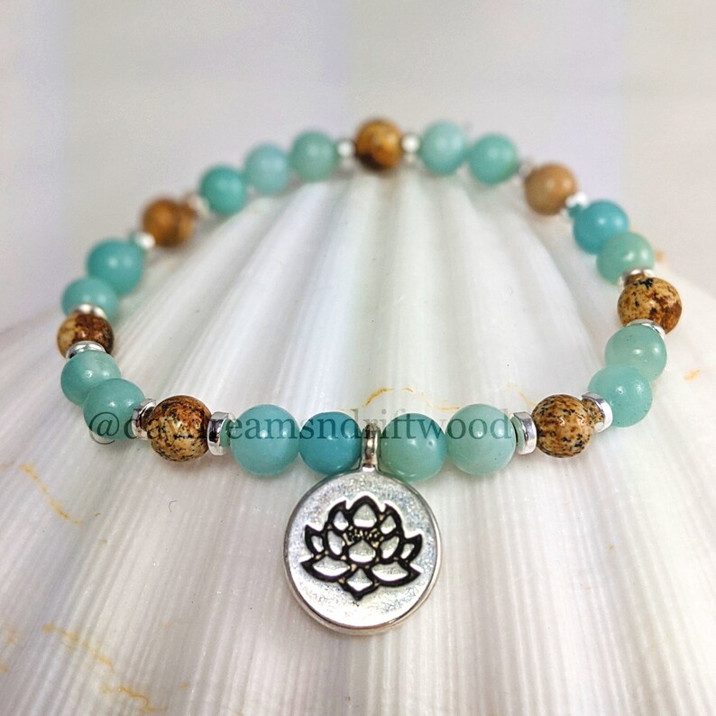 May include: A teal and brown beaded bracelet with a silver charm featuring a lotus flower design.
