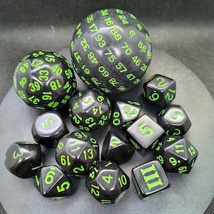 Puede incluir: Un conjunto de dados poliédricos negros con numeración verde brillante. El conjunto incluye varias formas, como esferas, cubos y pirámides, para juegos de rol. Los dados están dispuestos sobre una superficie oscura.