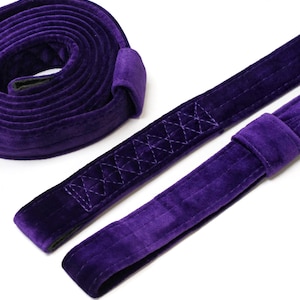 Peut inclure: Une sangle en velours violet profond dotée d'une texture douce et pelucheuse avec des coutures renforcées. La sangle est enroulée en forme circulaire d'un côté, avec deux sections plates étendues montrant des détails de points croisés.