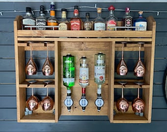 May include: A wooden wall-mounted bar with a shelf for bottles and a rack for glasses. The bar has three dispensers for liquor, with copper-colored glasses hanging below. The bottles on the shelf include Gentleman Jack, Jack Daniel's, and Wood's 100.