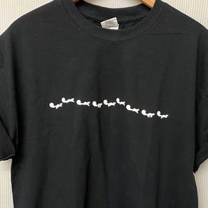 May include: Black t-shirt with a white graphic of a line of small white figures.