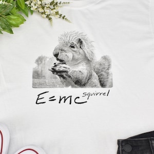 May include: White t-shirt with a black and white illustration of a squirrel holding a nut. The text "E=mc²squirrel" is printed below the illustration.