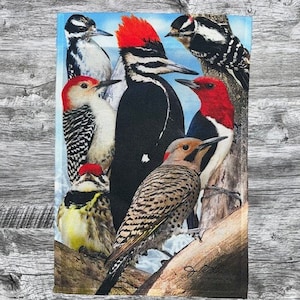 May include: A rectangular fabric featuring a vibrant illustration of various woodpeckers. The birds showcase a range of colors, including red, black, white, and brown, set against a backdrop of a blue sky and tree branches. The design is detailed and realistic.