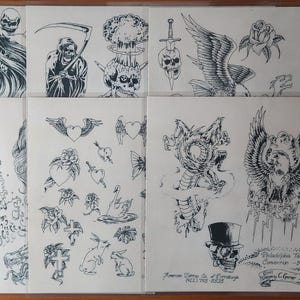 May include: A collection of tattoo flash art sheets with black and white designs. The sheets feature skulls, dragons, roses, eagles, and other traditional tattoo motifs. Some sheets include text, such as a shop name and phone number.