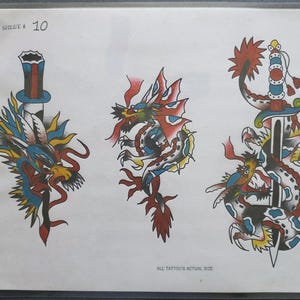 Può includere: Un foglio di disegni per tatuaggi con l'etichetta SHEET # 10 e ALL TATTOO'S ACTUAL SIZE. Presenta tre illustrazioni: un drago attorno a un cilindro, un drago singolo e un drago avvolto attorno a una spada. I disegni usano rosso, blu e giallo.