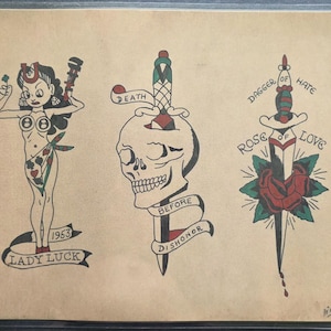 Può includere: Un foglio di carta beige con tre disegni per tatuaggi: una figura pin-up con un ferro di cavallo e una chiave inglese etichettata Lady Luck 1953, un teschio trafitto da un pugnale con il motto Death Before Dishonor e una rosa trafitta.