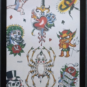 May include: A framed print showcasing classic tattoo flash designs. The artwork includes a heart pierced by a dagger, a spider with a human face, a devil, a skull in a top hat, and a banner that reads "Bing Bang Boom".