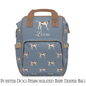 Puede incluir: Una mochila azul con un patrón repetitivo de perros pointer blancos y marrones. La bolsa tiene asas superiores y ribetes de color tostado, además de un bolsillo frontal. El nombre Liam está impreso en blanco sobre el bolsillo.