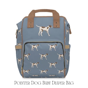 Puede incluir: Una mochila azul con un patrón repetitivo de perros pointer marrones y blancos. La bolsa incluye asas superiores de color tostado, un bolsillo frontal con cremallera y bolsillos laterales. El texto POINTER DOG BABY DIAPER BAG aparece abajo.