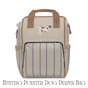 Può includere: Borsa per pannolini beige e marrone con un design a cane da caccia. La borsa presenta una tasca frontale, tasche laterali e una maniglia superiore. La borsa ha un motivo a righe verticali con una maniglia superiore e finiture marroni. Il testo "HUNTING POINTER DOG DIAPER BAG" è in basso.