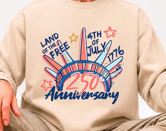 May include: Beige sweatshirt with a colorful graphic celebrating the 250th anniversary of the 4th of July. The design features the Statue of Liberty, stars, and the text "Land of the Free" and "1776".