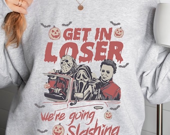 May include: Light gray sweatshirt with a Halloween-themed graphic. The design features the text "GET IN LOSER" above an image of three horror movie characters in a car, with the text "we're going slashing" below. Bats and pumpkins are also included.