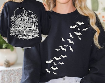 May include: Black sweatshirt with a white graphic of a haunted house and bats. The front of the sweatshirt has a graphic of bats flying in a diagonal line. The back of the sweatshirt has a graphic of a haunted house with a full moon and bats.