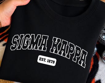 May include: A black crewneck sweatshirt featuring the white text SIGMA KAPPA in a collegiate font arched across the chest. Below the text is a white rectangular patch with rounded corners containing the black text EST. 1879 in a bold font.