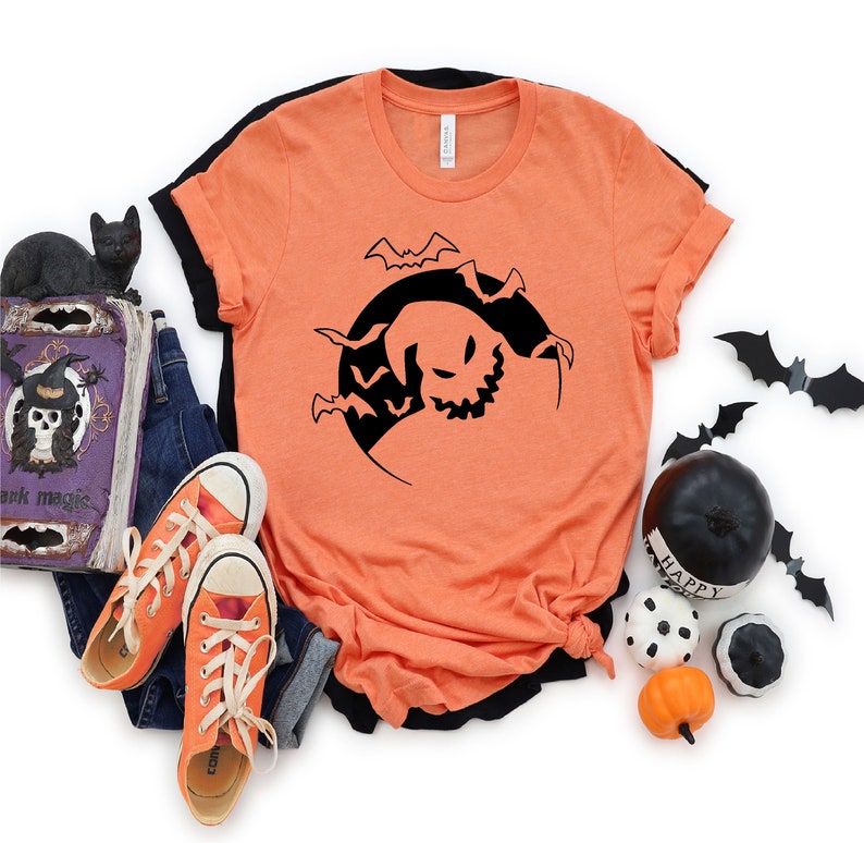 May include: Orange t-shirt featuring a black silhouette of a ghost with bats flying around it. The ghost is in a crescent moon shape.