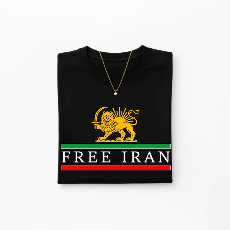 Może przedstawiać: Czarny t-shirt ze złotym lwem i słońcem, zielono-czerwonym paskiem i napisem "FREE IRAN". Złoty naszyjnik z wisiorkiem w kształcie gwiazdy jest zarzucony na koszulkę.