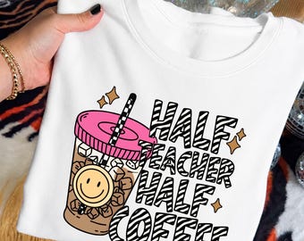 May include: A white crewneck sweatshirt featuring a graphic of an iced coffee in a clear cup with a pink lid, a black and white striped straw, and a yellow smiley face. The text reads "HALF TEACHER HALF COFFEE" in black and white zebra print.