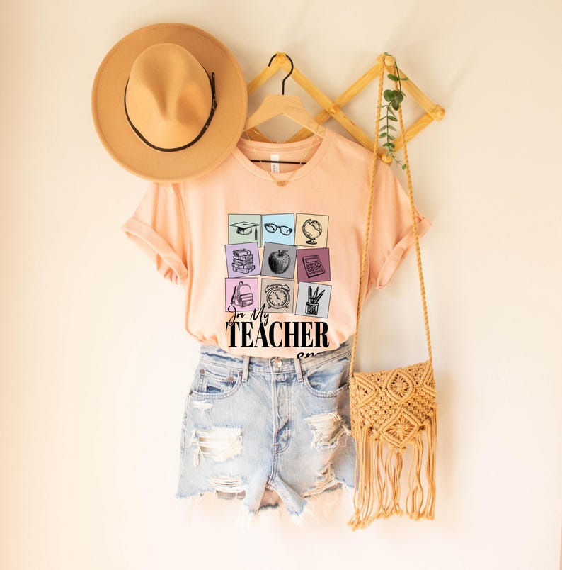 May include: Peach colored t-shirt with a graphic of school supplies in squares and the text "In My Teacher Zone".