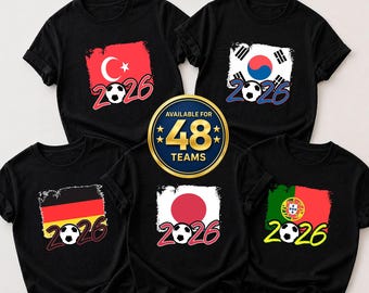 May include: Black t-shirts with country flag designs and the year 2026. Flags include Turkey, South Korea, Germany, Japan, and Portugal. A gold emblem states "Available for 48 Teams". Soccer ball graphics are also present.
