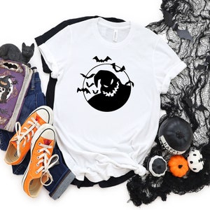 May include: White t-shirt featuring a black silhouette of a grinning ghost with bats flying around it. The ghost is in a circle, resembling a full moon.