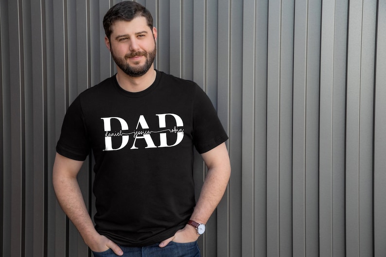 May include: A black t-shirt with the word "DAD" printed in white. The names "Daniel", "Jessica", and "Robin" are written in a smaller font size underneath the word "DAD".