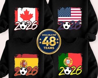 May include: Black sweatshirts with soccer-themed designs. Each sweatshirt features a flag and the year 2026, with a soccer ball graphic. Flags include Canada, the USA, Spain, and Portugal. A central emblem reads "Available for 48 Teams."
