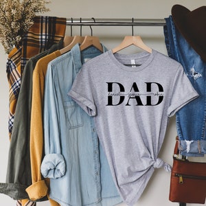 May include: Gray t-shirt with the word "DAD" in black block letters. The names "Daniel", "Jessica", and "Robin" are written in cursive script above the word "DAD".