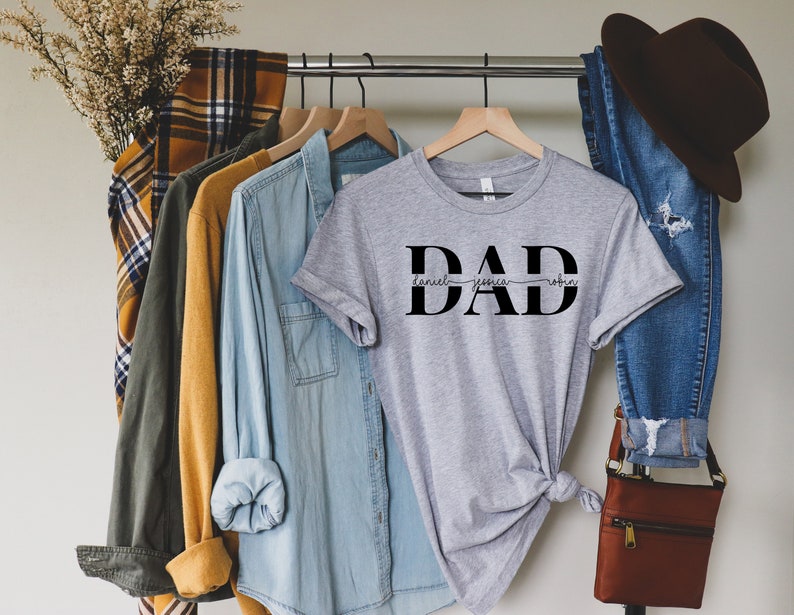May include: Gray t-shirt with the word "DAD" in black block letters. The names "Daniel", "Jessica", and "Robin" are written in cursive script above the word "DAD".