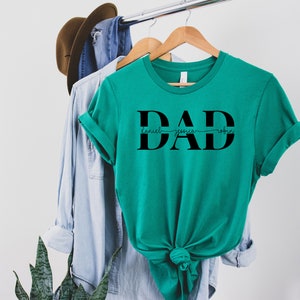 May include: Teal t-shirt with the word "DAD" in large black letters. The names "Daniel", "Jessica", and "Robin" are written in a smaller font size underneath the letters.