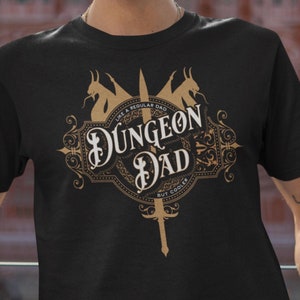 May include: Black t-shirt with a gold graphic of a sword and a crest that says "Dungeon Dad, Like a Regular Dad But Cooler".
