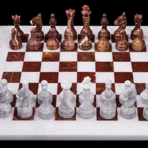 May include: A complete chess set with a marble board and stone pieces. The board features a white and red checkered pattern. The chess pieces are in shades of brown and white.
