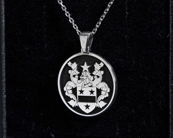 May include: A silver necklace with a round pendant featuring a black and white coat of arms design. The necklace is displayed in a black velvet box.