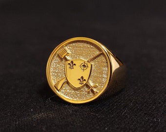 May include: A gold ring with a shield and crossed oars design. The shield has three fleur-de-lis.
