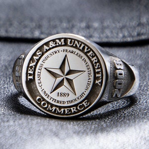 May include: A white ceramic mug with a black handle and the text "But First, Coffee" in a black, bold font. The mug is sitting on a white surface. The mug is approximately 4 inches tall.