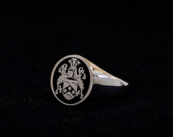 Può includere: Un anello a sigillo d'argento con un ovale in smalto nero con uno stemma inciso in bianco.