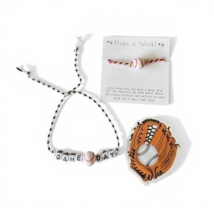 May include: A baseball-themed gift set featuring a black and white beaded bracelet with "GAME DAY" spelled out, a baseball charm bracelet, and a baseball glove sticker. The set includes a card that reads "Make a Wish!"